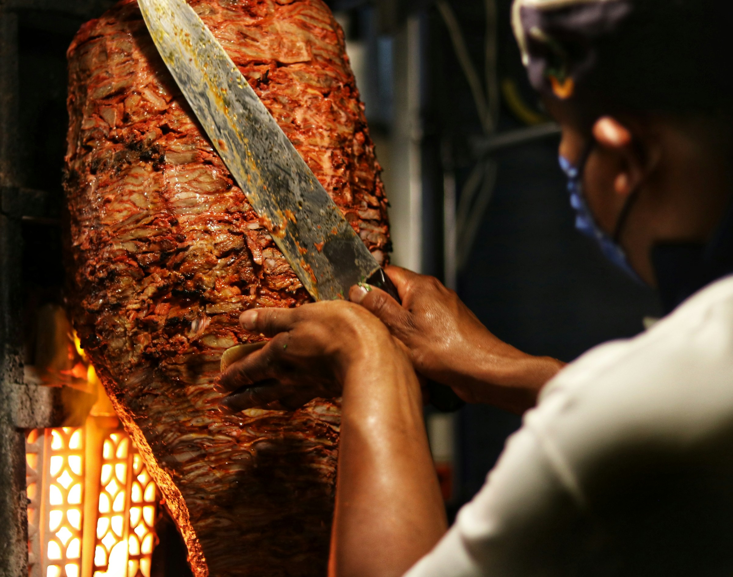A chef carving meat from a large vertical spit