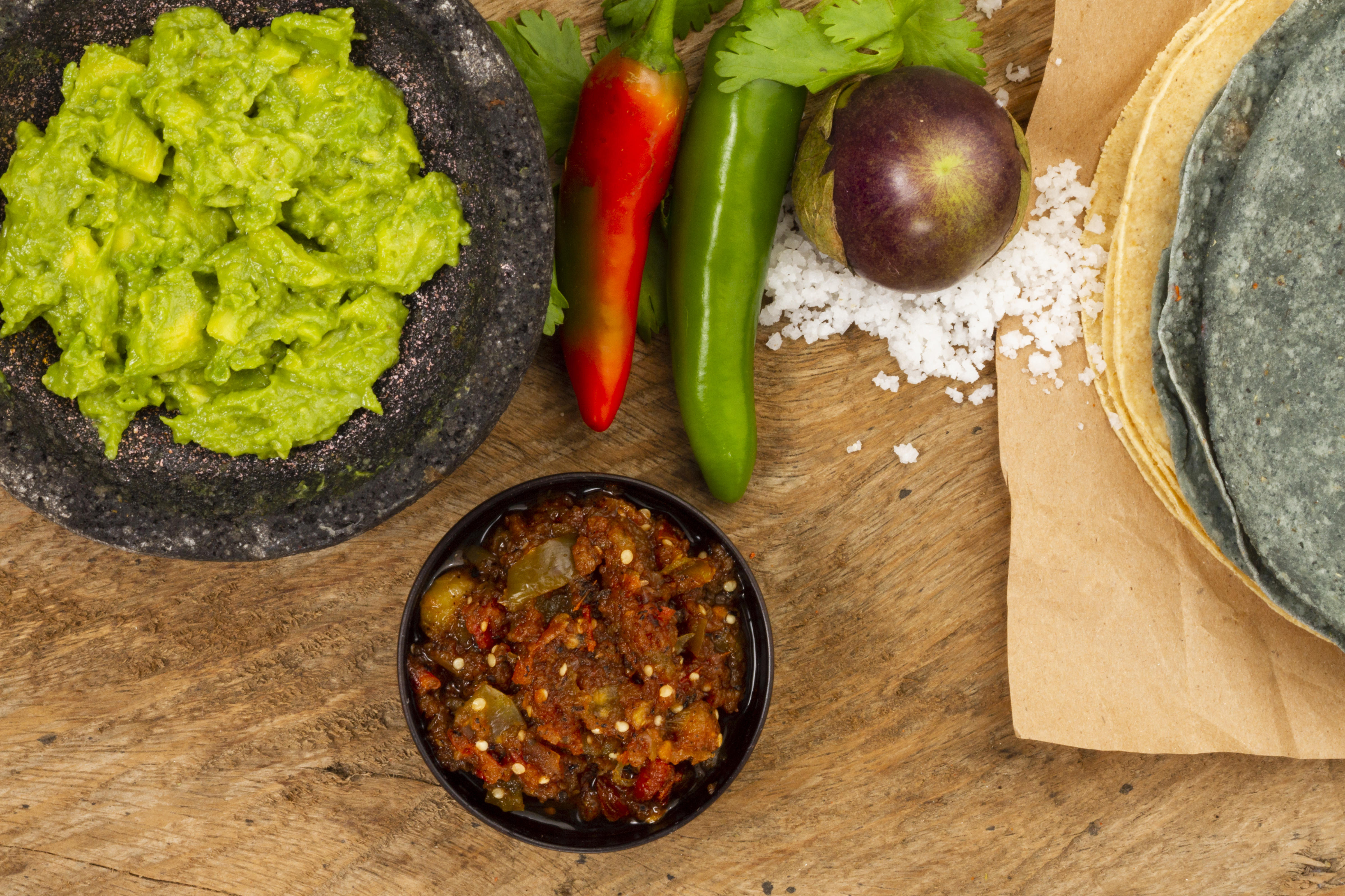 A bowl of red salsa next to a bowl of guacamole and tortilla chips.